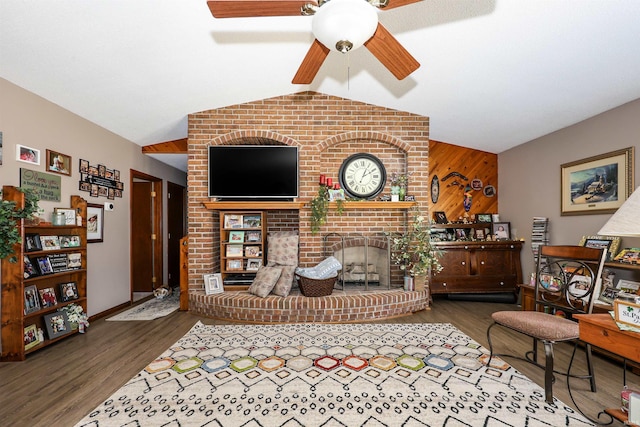 living room featuring wooden walls, an accent wall, lofted ceiling, wood finished floors, and a ceiling fan