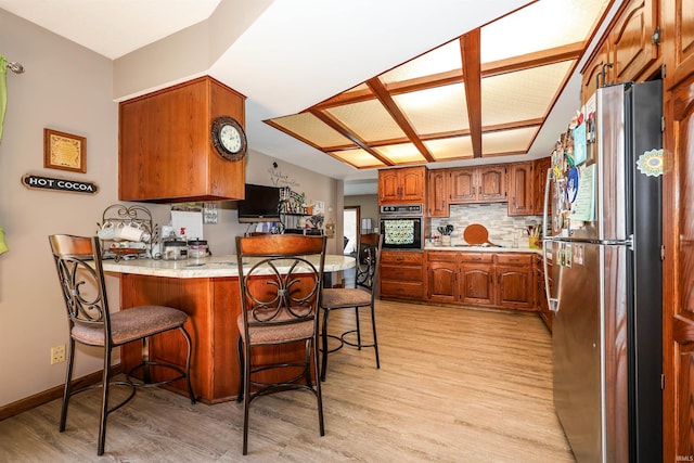 kitchen with black oven, a kitchen bar, decorative backsplash, a peninsula, and freestanding refrigerator