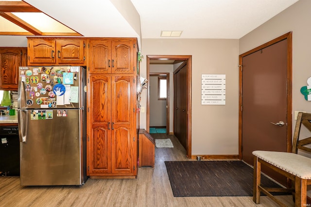 kitchen featuring light wood-style flooring, freestanding refrigerator, brown cabinetry, baseboards, and dishwasher