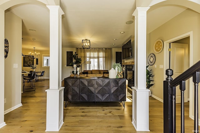 interior space with a glass covered fireplace, baseboards, light wood-type flooring, and ornate columns