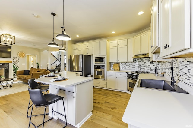 kitchen with light wood finished floors, a kitchen island, under cabinet range hood, decorative backsplash, and stainless steel appliances