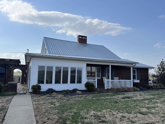 view of front of property featuring a front lawn, metal roof, covered porch, and a chimney