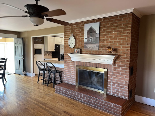 living area with a fireplace, wood finished floors, baseboards, and ceiling fan