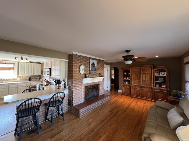 living area featuring a brick fireplace, wood finished floors, and a ceiling fan