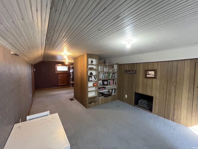 finished basement featuring visible vents, wooden walls, carpet flooring, and a fireplace