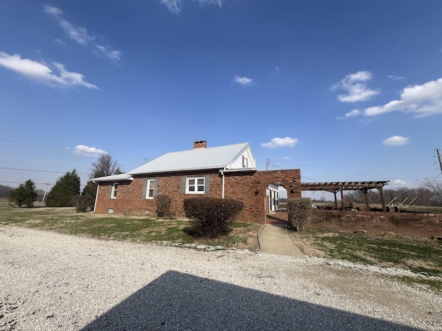 view of property exterior featuring metal roof, brick siding, a chimney, and a pergola