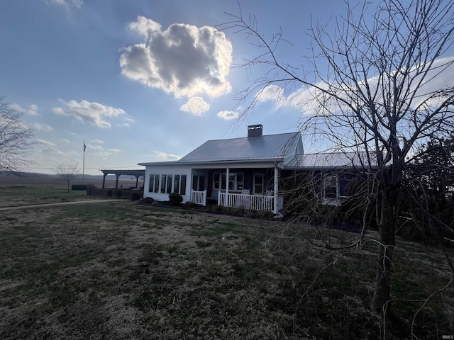 view of front of property featuring a porch, metal roof, a front yard, and a chimney