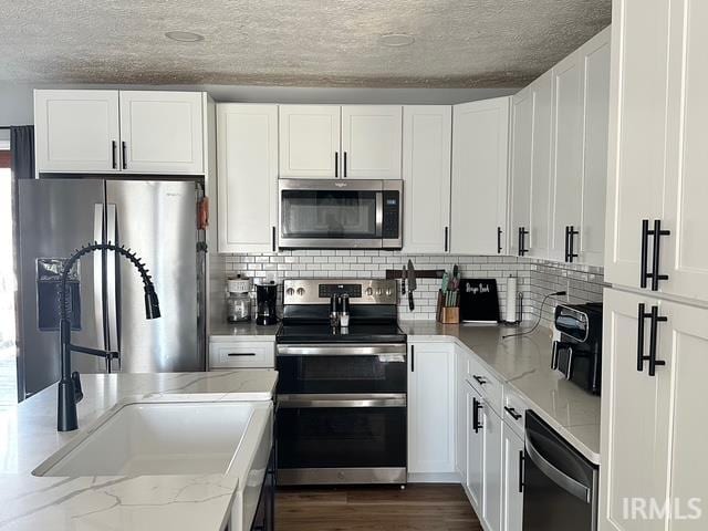 kitchen featuring white cabinets, light stone counters, appliances with stainless steel finishes, and a sink