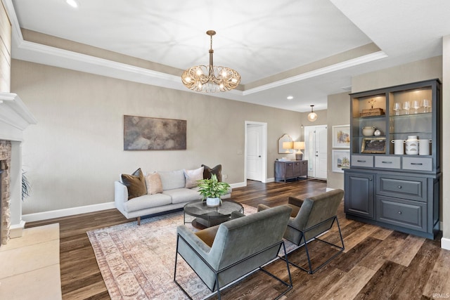 living room with dark wood-type flooring, a tray ceiling, a fireplace, baseboards, and a chandelier