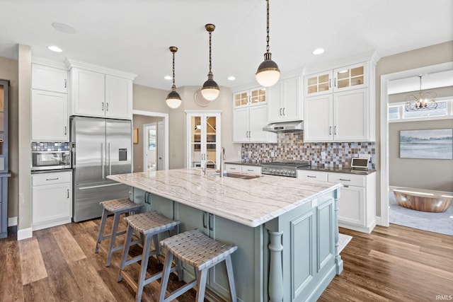 kitchen with under cabinet range hood, appliances with stainless steel finishes, wood finished floors, and a sink