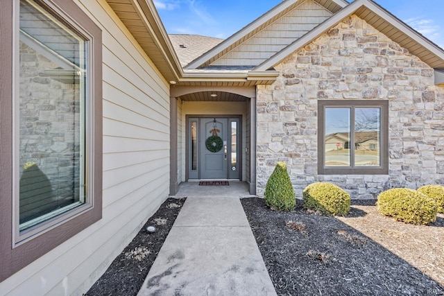 doorway to property with stone siding and roof with shingles