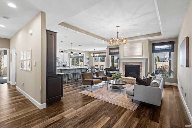 living room featuring a tray ceiling, baseboards, a notable chandelier, and dark wood finished floors