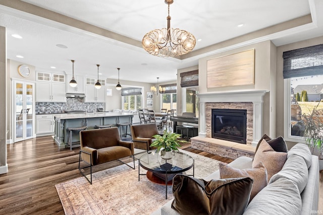 living area featuring dark wood finished floors, a tray ceiling, recessed lighting, a fireplace, and an inviting chandelier