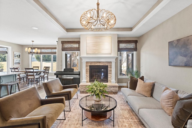 living area with baseboards, a chandelier, a fireplace, wood finished floors, and a raised ceiling