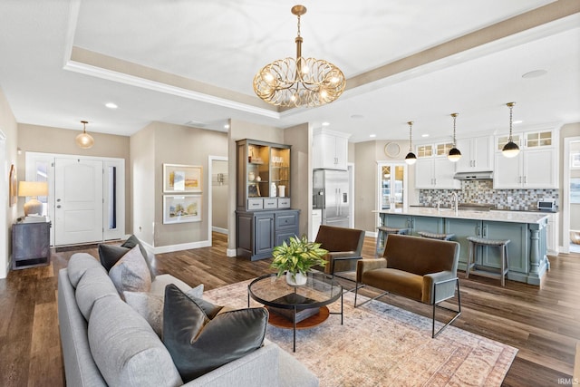 living room featuring a tray ceiling, baseboards, a notable chandelier, and dark wood-style flooring