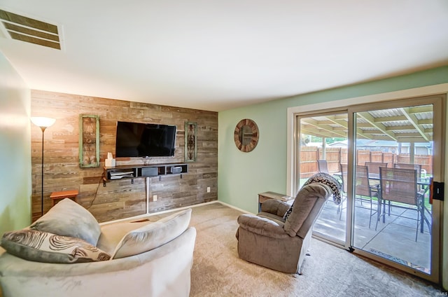 carpeted living area with an accent wall, baseboards, visible vents, and wood walls