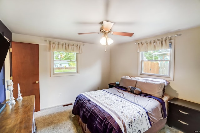 carpeted bedroom with visible vents, multiple windows, and ceiling fan