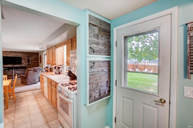 kitchen with a sink, open floor plan, white appliances, wooden walls, and light countertops