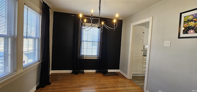 unfurnished dining area featuring baseboards, wood finished floors, and a chandelier