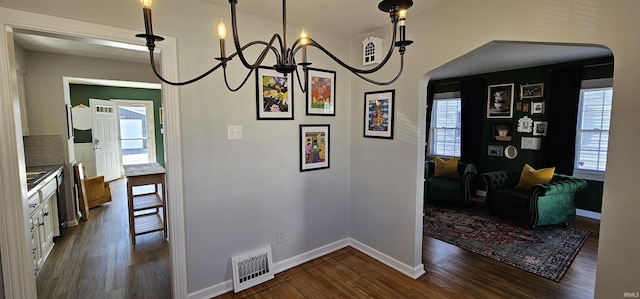 interior space featuring dark wood-type flooring, arched walkways, visible vents, and baseboards