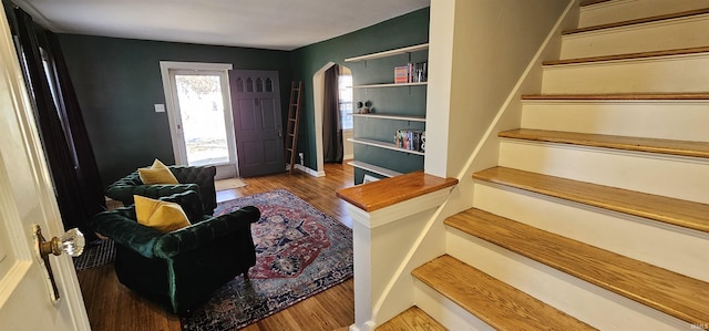 foyer entrance featuring stairs, wood finished floors, arched walkways, and baseboards