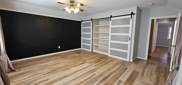 unfurnished bedroom with a barn door, wood finished floors, and baseboards