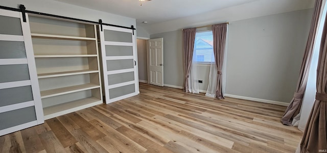 unfurnished bedroom with a barn door, wood finished floors, and baseboards