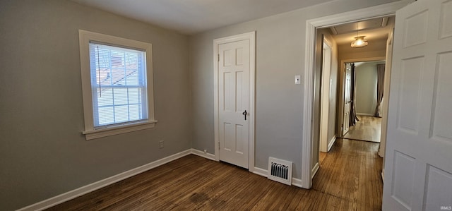 unfurnished bedroom featuring visible vents, dark wood finished floors, a closet, baseboards, and attic access