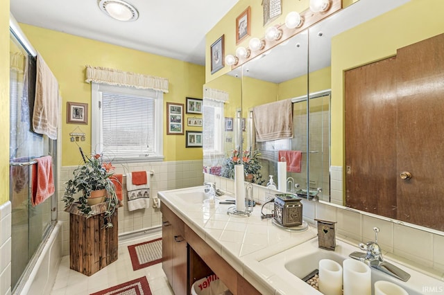 full bathroom featuring tile walls, double vanity, a wainscoted wall, and a sink