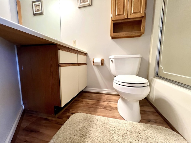 bathroom with baseboards, bath / shower combo with glass door, toilet, wood finished floors, and vanity