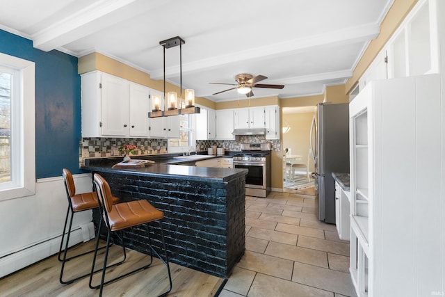 kitchen with under cabinet range hood, a sink, dark countertops, appliances with stainless steel finishes, and a peninsula