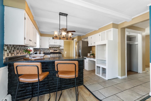 kitchen with a peninsula, under cabinet range hood, appliances with stainless steel finishes, beamed ceiling, and backsplash