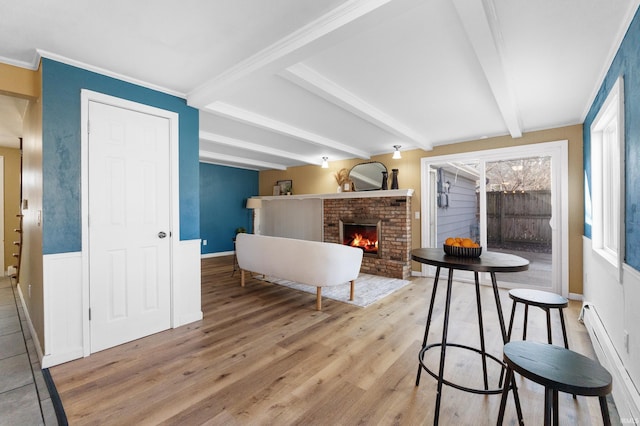 interior space featuring light wood-type flooring, beamed ceiling, ornamental molding, a baseboard heating unit, and a fireplace