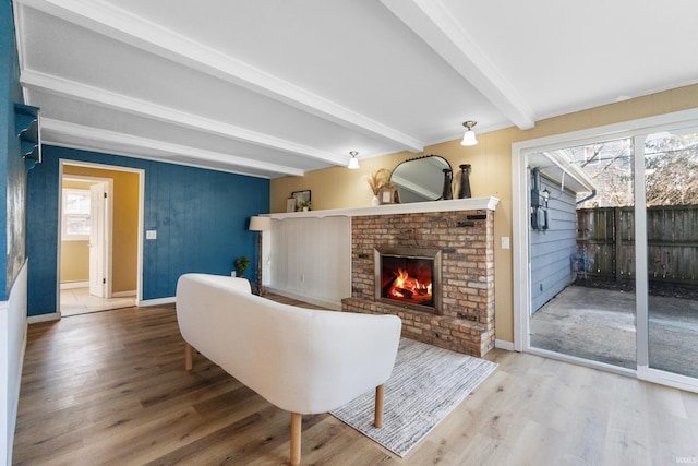 living area featuring a fireplace, beam ceiling, wood finished floors, and baseboards