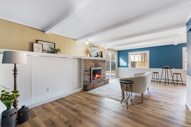 living area with beam ceiling, baseboard heating, wood finished floors, and a fireplace