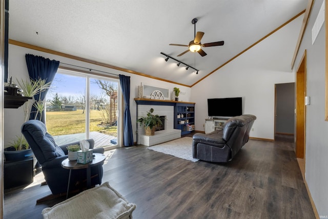 living room with a ceiling fan, dark wood finished floors, vaulted ceiling, crown molding, and a brick fireplace