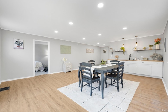 dining room featuring visible vents, wet bar, light wood-style flooring, recessed lighting, and ornamental molding