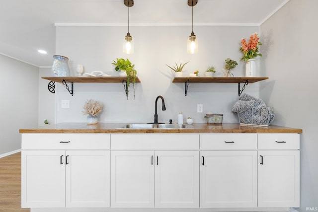 bar featuring a sink, crown molding, light wood finished floors, baseboards, and hanging light fixtures