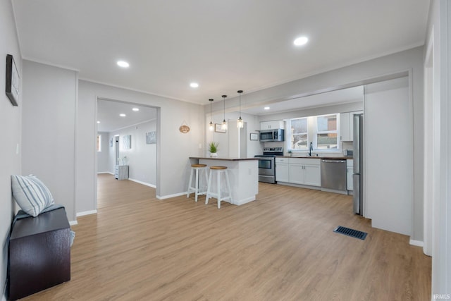 kitchen featuring visible vents, a kitchen breakfast bar, dark countertops, appliances with stainless steel finishes, and light wood finished floors