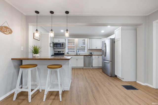 kitchen featuring visible vents, a breakfast bar, a sink, stainless steel appliances, and a peninsula