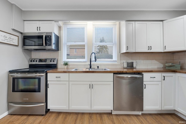 kitchen featuring light wood-style flooring, a sink, backsplash, white cabinetry, and appliances with stainless steel finishes