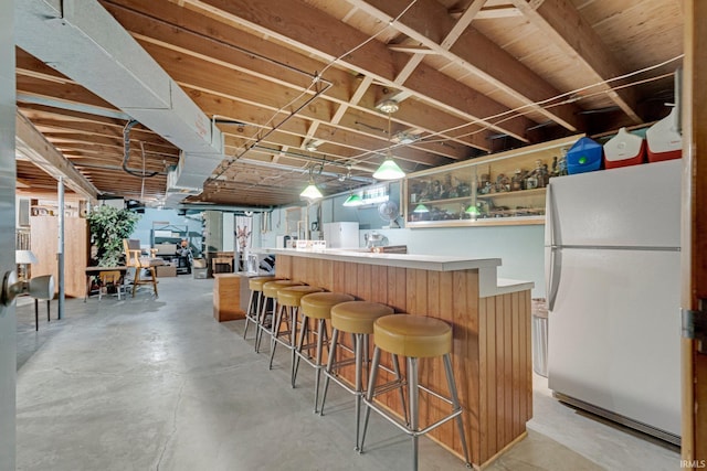 bar featuring a community bar, concrete floors, hanging light fixtures, and freestanding refrigerator