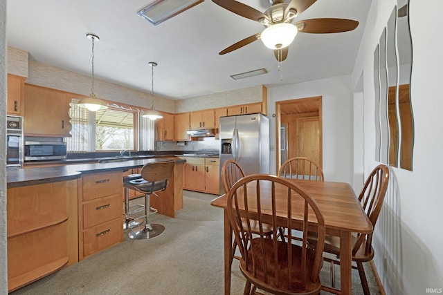 kitchen with a breakfast bar area, a ceiling fan, appliances with stainless steel finishes, under cabinet range hood, and dark countertops