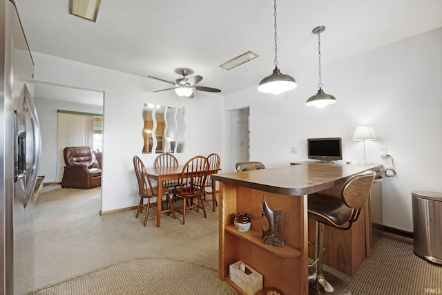 kitchen with dark countertops, open floor plan, light colored carpet, a kitchen bar, and stainless steel fridge