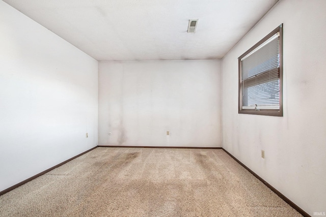 spare room featuring light colored carpet, visible vents, and baseboards