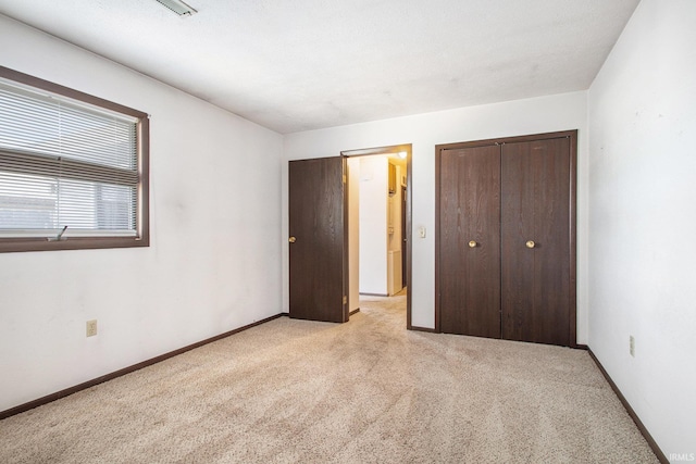 unfurnished bedroom featuring a closet, light carpet, and baseboards