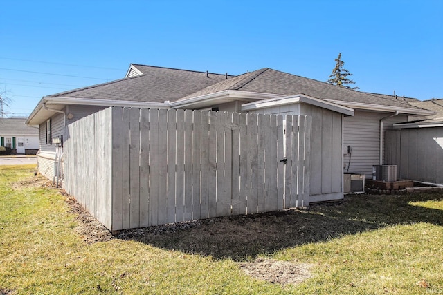 view of side of property with central air condition unit, a lawn, roof with shingles, and fence