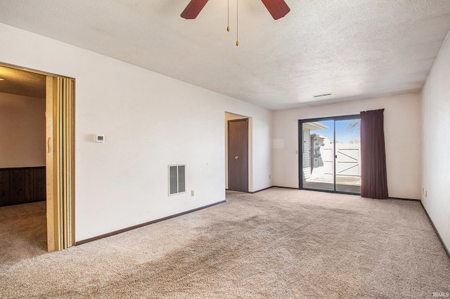 carpeted empty room with a textured ceiling, baseboards, visible vents, and ceiling fan