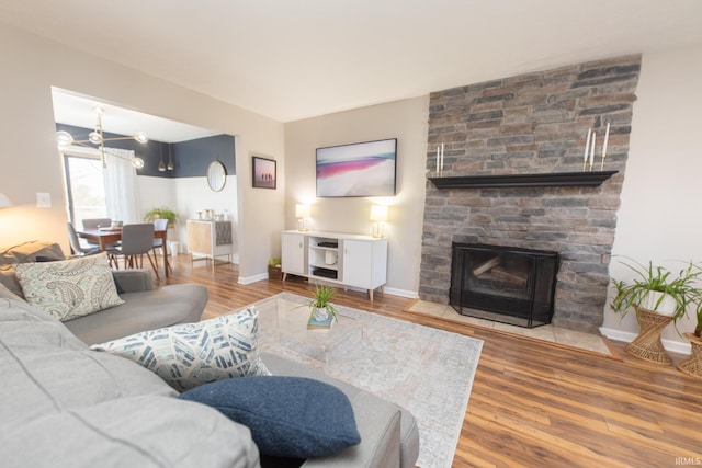 living room featuring a stone fireplace, an inviting chandelier, wood finished floors, and baseboards