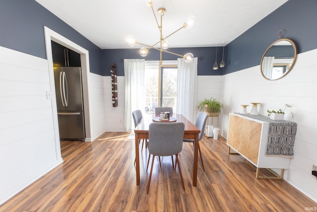 dining space featuring a wainscoted wall, wood finished floors, and a chandelier